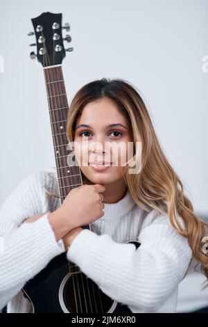 Die Gitarre zu spielen ist das, was mich glücklich macht. Eine junge Frau, die mit ihrer Gitarre zu Hause sitzt. Stockfoto