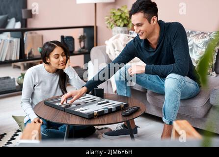 Eine Runde Spaß auf dem Haus. Ein junges Paar spielt zu Hause ein Backgammon-Spiel. Stockfoto