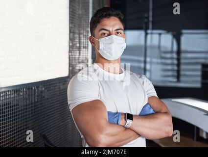 Es ist meine Aufgabe, dafür zu sorgen, dass alle in dieser Einrichtung sicher bleiben. Porträt eines jungen Mannes, der eine Gesichtsmaske in einem Fitnessstudio trägt. Stockfoto