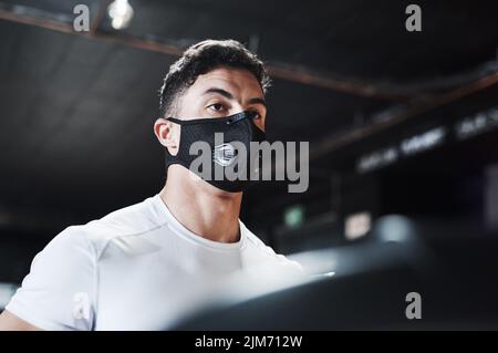 Gesundheit und Sicherheit. Ein hübscher und sportlicher junger Mann, der beim Training im Fitnessstudio eine Maske trägt. Stockfoto