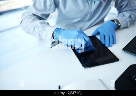 Während der Pandemie ist Sauberkeit besonders wichtig. Nahaufnahme eines nicht erkennbaren Geschäftsmannes, der ein digitales Tablet in einem Büro reinigt. Stockfoto