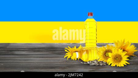 Flaschen Sonnenblumenöl und Samen auf Holztisch gegen die Flagge der Ukraine Stockfoto