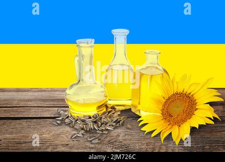 Flaschen Sonnenblumenöl und Samen auf Holztisch gegen die Flagge der Ukraine Stockfoto