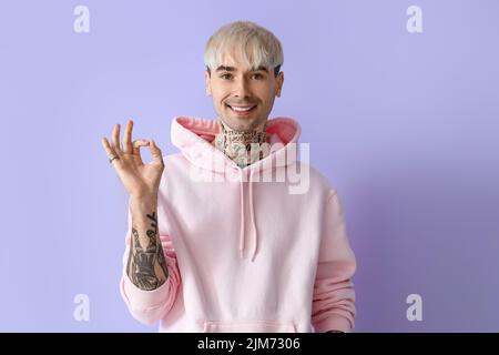 Junger tätowierter Mann in pinkem Hoodie mit OK auf fließendem Hintergrund Stockfoto