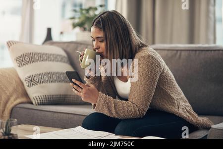 Verlängern Sie die Lebensdauer Ihres Gehaltsschecks mit intelligenter Finanzplanung. Eine junge Frau, die Kaffee trinken und ein Smartphone benutzen, während sie Papierkram durchläuft Stockfoto