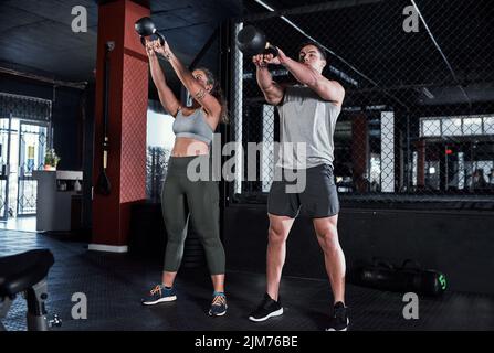 Gemeinsam Kraft und Ausdauer verbessern. Zwei sportliche junge Menschen trainieren mit Kettlebells im Fitnessstudio. Stockfoto