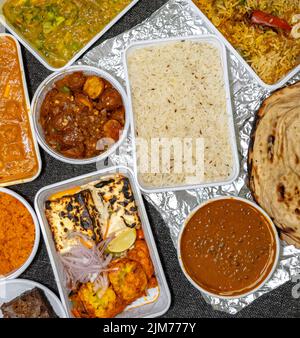 Draufsicht auf eine Vielzahl von indischen Speisen zum Mitnehmen in weißen Kunststoffbehältern auf einem Stoffhintergrund. Stockfoto