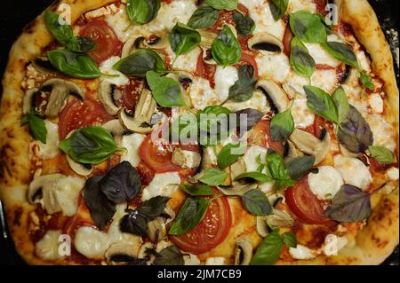 Draufsicht. Hausgemachte, frisch gebackene italienische Pizza mit Mozzarella, Tomaten und Basilikumblättern. Nahaufnahme, selektiver Fokus. Stockfoto