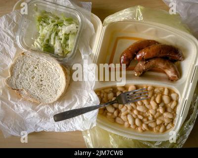 Essen zum Mitnehmen in Styroporverpackung - weiße Bohnen und Würstchen mit zerkleinerten Kohlsalat, Draufsicht Stockfoto