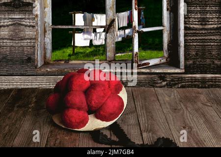 Original Schwarzwälder Bollenhütte auf einem Holztisch vor einem Holzfenster mit Blick in den Garten Stockfoto