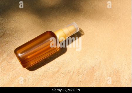 Dunkle Flasche ohne Marke mit SPF-Öl oder Sonnencreme auf goldenem Sandstrand. Sommerliches Kosmetikkonzept. Stockfoto