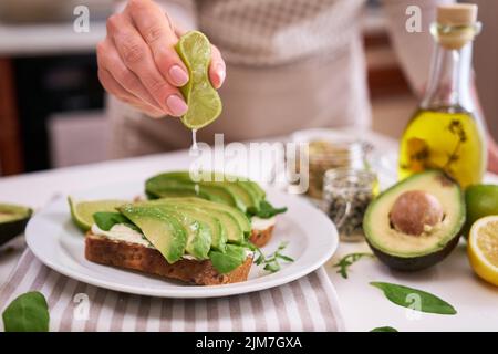 Frau quetscht frischen Limettensaft auf einem Avocado und Frischkäse-Toast Stockfoto