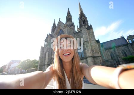 Lächelndes Touristenmädchen porträtiert sich selbst vor der Salford Cathedral, Manchester, England Stockfoto