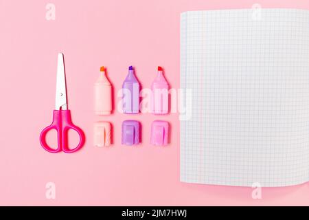 Zurück zur Schule. Komposition mit geöffnetem Copybook, Markern und Scheren auf rosa Hintergrund. Flach liegend. Modell. Stockfoto