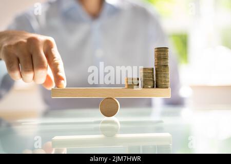 Geschäftsmann Balancing gestapelte Münzen mit Finger auf Holz- Wippe Stockfoto