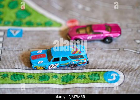 Ein selektiver Fokus auf eine Mischung aus Mattel Hot Wheels Spielzeugmodell blauem Auto mit der Nummer 2 darauf auf einer Spielmatte Stockfoto