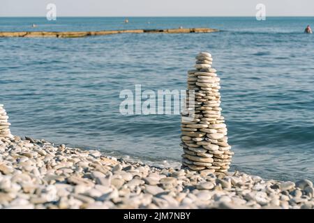 Ausgewogene Steine an einem Kieselstrand. Am Strand in einer Balancepyramide angeordnete Seesteine. Meditation und Harmonie. Verschwommener Meereshintergrund. Stockfoto