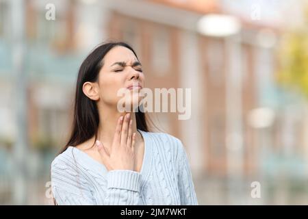 Gestresste Frau mit Halsschmerzen, die auf der Straße steht Stockfoto