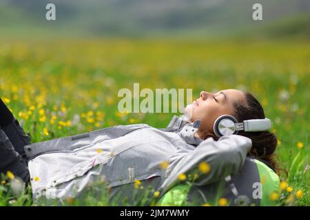 Wanderer, der Kopfhörer trägt, hört Musik und entspannt auf dem Gras auf einem Feld in den Bergen Stockfoto