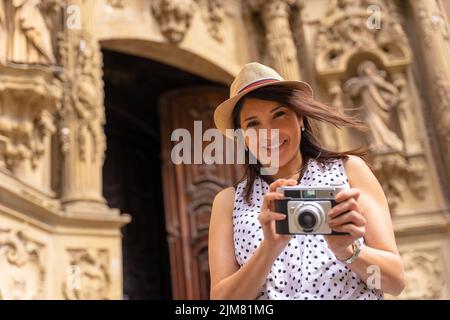 Eine hispanische Touristin mit Hut besucht eine Kirche und fotografiert mit einer Kamera Stockfoto