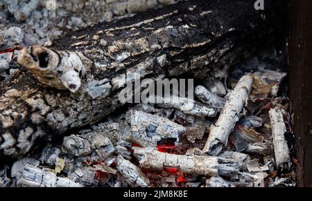 Schwelende Holzkohle in einem Grill. Vereinzelte Stücke Glut im Herd gemischt mit Asche. Asche nach dem Essen im Freien vorzubereiten Stockfoto