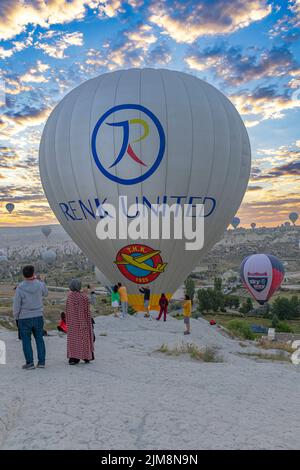 GOREME/TÜRKEI - 30. Juni 2022: Heißluftballon fliegt in der Nähe der Touristen über die Hügel von goreme. Stockfoto