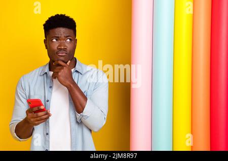 Foto von nachdenklichen Kerl verwenden Gerät zögern Bestellung Lieferung gemalt Rollen isoliert Glanz Farbe Hintergrund Stockfoto