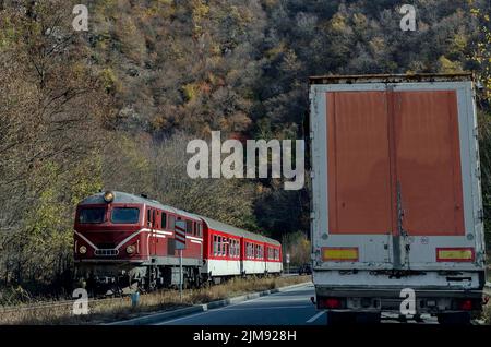 Die Strecke der Schmalspurbahn und des Zuges mit roter Lokomotive und Wagen kommt vom Septemvri Bahnhof nach Dobrinishte über den Rhodope Mountan Stockfoto