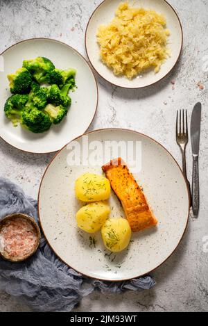 Hausgemachter gebackener Lachs serviert mit Kartoffeln, Brokkoli und Sauerkraut Stockfoto