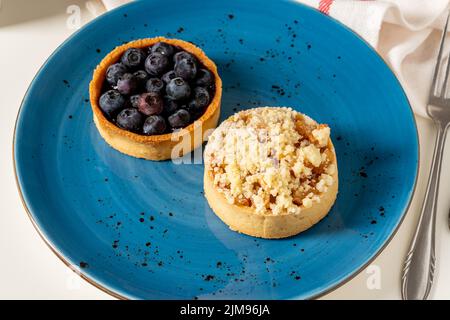 Frisch gebackene einporige Heidelbeer- und Apfelkuchen auf einem blauen Porzellanteller Stockfoto