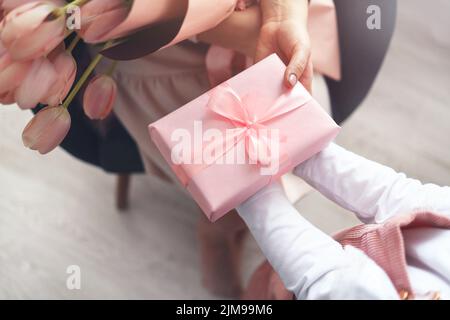 Kinderhände halten schöne rosa Geschenkbox mit Band und rosa Tulpenblume. Draufsicht, Nahaufnahme. Vorbereitung auf die Feiertage. Stockfoto