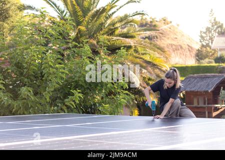Junge Frau techinician hart arbeiten und konzentriert sich in einer Solarpanel-Installation mit einem elektrischen Schraubendreher zur Hand Stockfoto