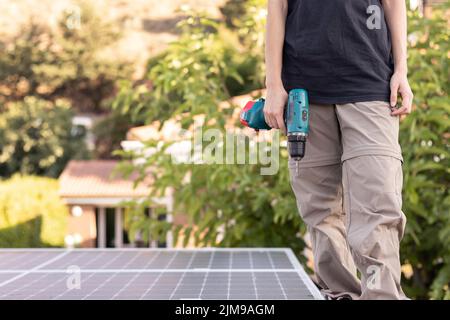 Beschnittene Ansicht einer jungen Frau, die an einem Solarpanel-Kraftwerk arbeitet und einen elektrischen Schraubendreher hält, während sie stehend läuft Stockfoto