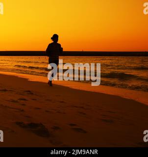 Frau joggt während des Sonnenuntergangs über dem Jumeira Beach in Dubai. Stockfoto