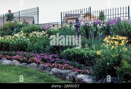 Statue des heiligen Franziskus von Assisi unter den schönen blühenden Lilien und Pflanzen an einem Sommerabend in den Panola Valley Gardens in Lindstrom, Minnesota Stockfoto