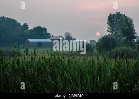 Farm bei Sonnenuntergang mit Dunst durch rauchigen Himmel von Waldbränden in den westlichen Vereinigten Staaten und Kanada brennen. Aufgenommen in Chisago City, Minnesota, USA. Stockfoto