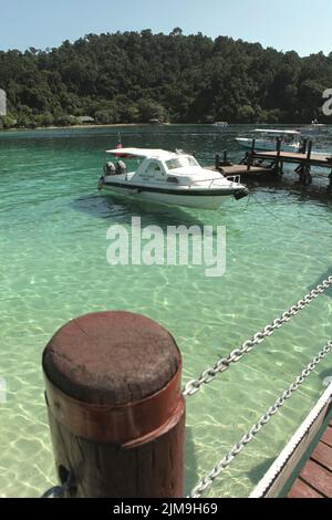 Ein Touristenboot auf dem Küstenwasser, von einem Steg auf Pulau Sapi (Sapi Island) aus gesehen, einem Teil des Tunku Abdul Rahman Parks in Sabah, Malaysia. Stockfoto