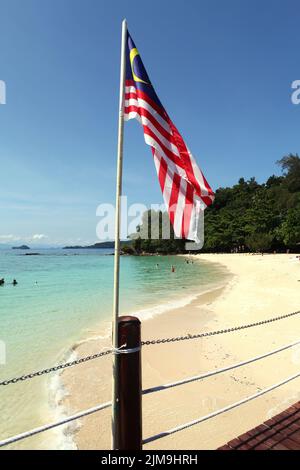 Nationalflagge Malaysias im Hintergrund eines Strandes auf Pulau Sapi (Sapi Island), einem Teil des Tunku Abdul Rahman Parks in Sabah, Malaysia. Stockfoto