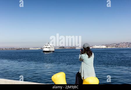 Frau, die Fotos von der Bucht von San Diego gemacht hat, während sie sich am Pier hingesetzt hat Stockfoto