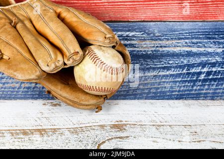 Alt abgenutzter Baseballhandschuh und Ball auf verblassten Brettern, die in amerikanischen Nationalfarben gestrichen sind Stockfoto