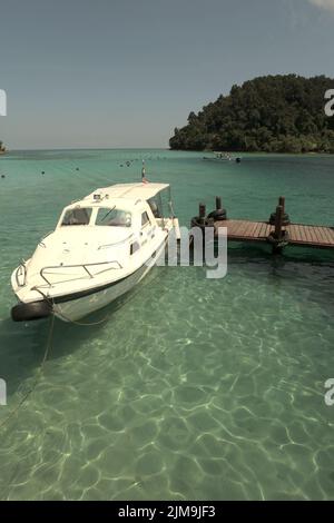 Ein Touristenboot auf dem Küstenwasser, von einem Steg auf Pulau Sapi (Sapi Island) aus gesehen, einem Teil des Tunku Abdul Rahman Parks in Sabah, Malaysia. Stockfoto