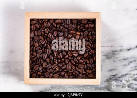 Frisch geröstete Kaffeebohnen in Holzkiste auf Marmorsteinboden Stockfoto