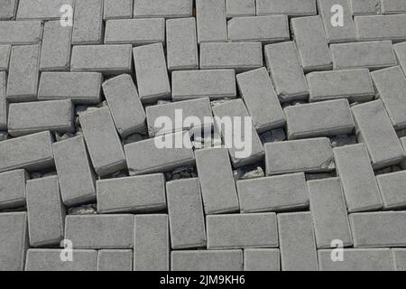 Verrenkter, aus Beton gefertigter Straßenbeläge; gebrochener, unebener Weg; verrenktes Ziegelmuster und -Struktur; horizontaler städtischer Hintergrund und Kopierraum. Stockfoto