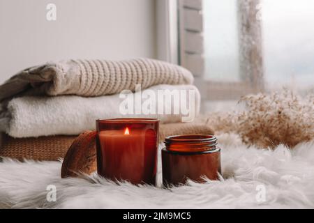 Zwei Kerzen auf der Fensterbank mit Pullovern. Herbststimmung. Stockfoto