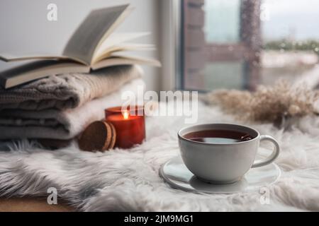 Wunderschöne Herbstkomposition mit brennender Kerze und einer Tasse Tee auf der Fensterbank Stockfoto