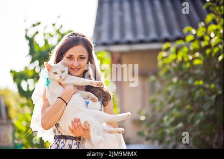 Mädchen-Braut hält auf Händen weiße Katze mit anderen farbigen Augen Stockfoto