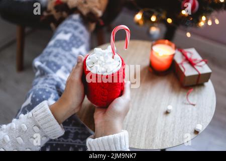 Ein Mädchen hält eine Tasse Kakao mit Sümpfen und Süßigkeiten in den Händen. Gemütliche Neujahrsstimmung. Stockfoto