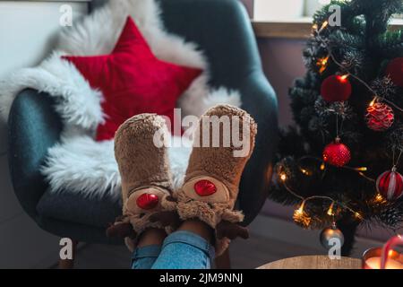 Füße in niedlichen Pantoffeln auf dem Hintergrund des Weihnachtsbaums. Stockfoto