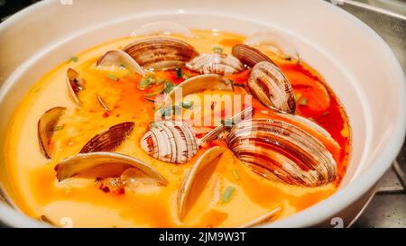 Eine Nahaufnahme einer Kimchi-Suppe mit Venusmuscheln in einer weißen Schüssel auf dem Tisch Stockfoto