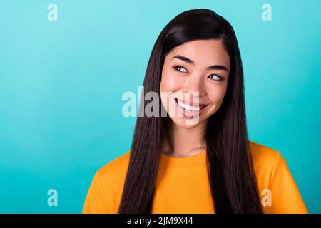 Foto von wunderschönen guten Laune Mädchen mit geraden Frisur gekleidet gelben T-Shirt Blick auf leeren Raum isoliert auf türkisfarbenem Hintergrund Stockfoto